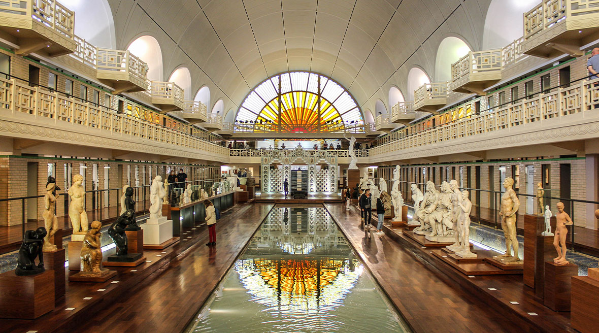 art deco style swimming pool with stained glass windows and marble statues lining the pool edge